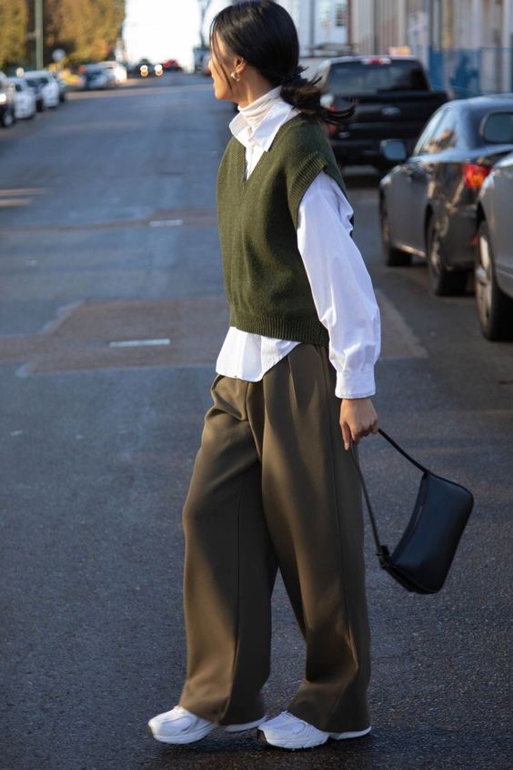 a neutral turtleneck, a white shirt, a green waistcoat, brown trousers and a black bag plus white trainers