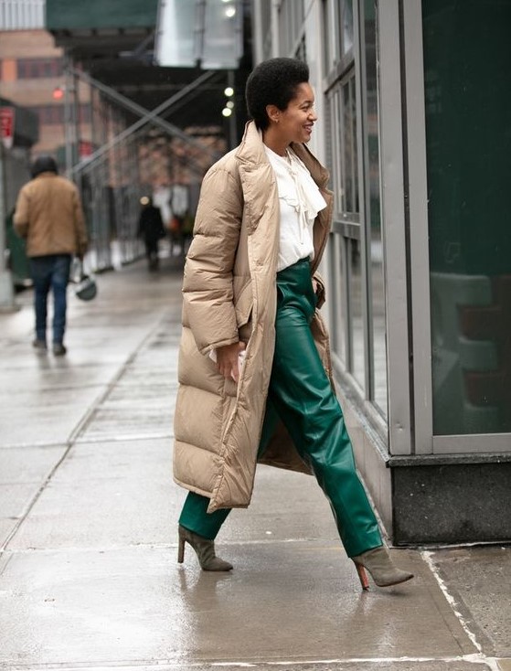 a refined winter look with a white blouse with a bow, emerald leather rousers, grey suede boots, a tan puffer coat