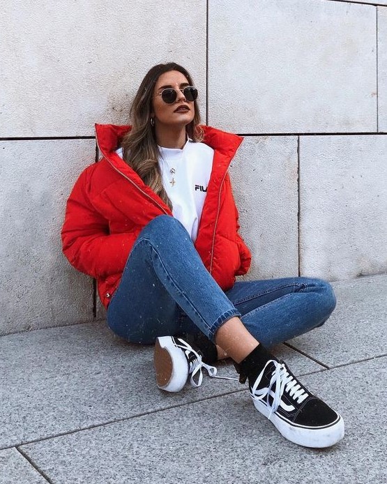a sporty outfit with a white tee, blue skinnies, a red puffer jacket and black sneakers and socks