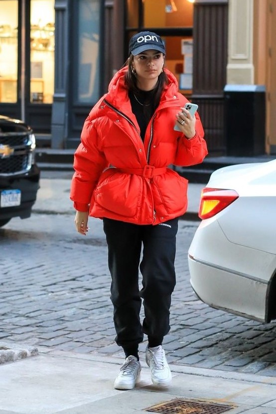 a sporty winter look with a black turtleneck, joggers, white trainers, a red puffer jacket with a belt and cap