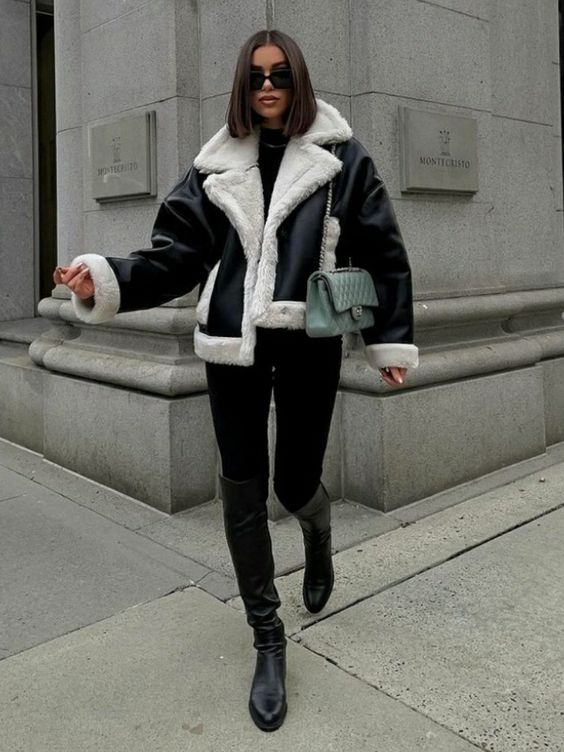 a stylish and elegant winter outfit with a black turtleneck and leggings, black boots and a shearling jacket plus a green bag