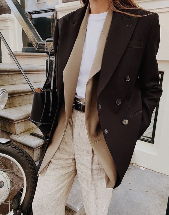 a stylish layered winter wotk outfit with a white t-shirt, neutral trousers, a tan blazer, a black cropped coat and a black bag