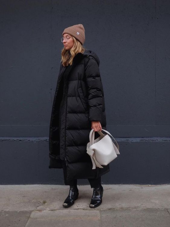 a total black outfit with trousers and a hoodie, boots, a puffer coat, a white bag and a brown beanie