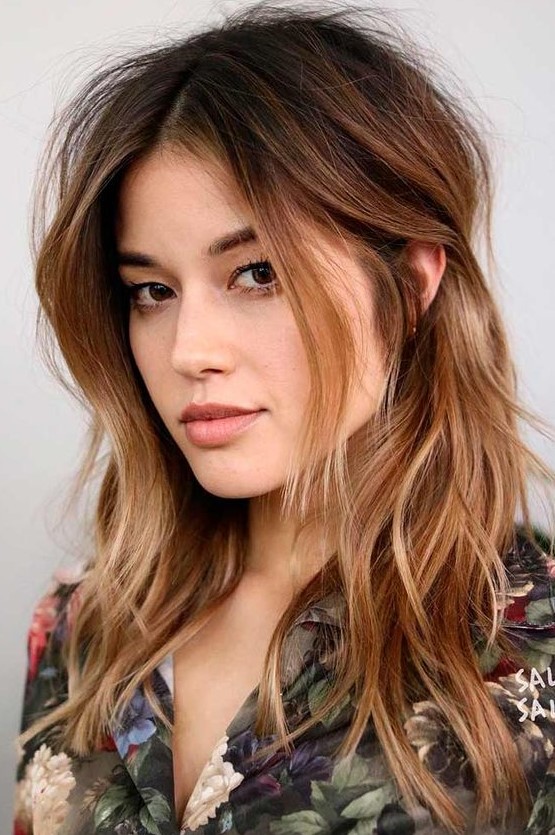 dark brown root plus ombre caramel ends and messy waves plus layered bangs looks bold and catchy