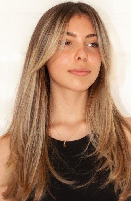 long light brown hair with caramel balayage and long curtain bangs adding interest to the look