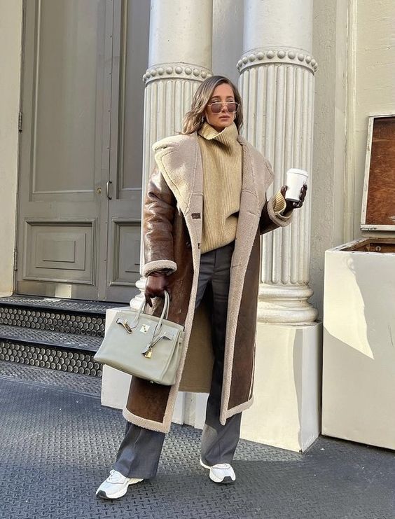 a beige sweater, grey pants, white trainers, a brown shearling coat, a grey bag and sunglasses for winter