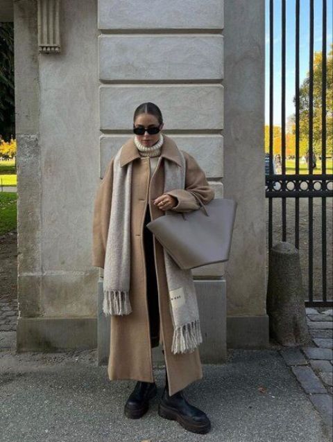 a cold weather outfit with a white sweater, black jeans and chunky boots, a beige maxi coat, a neutral scarf and a greige tote