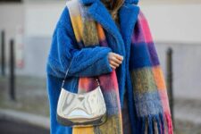 a colorful winter look with grey jeans, a bold blue teddy coat, a colorful scarf with fringe and a silver bag