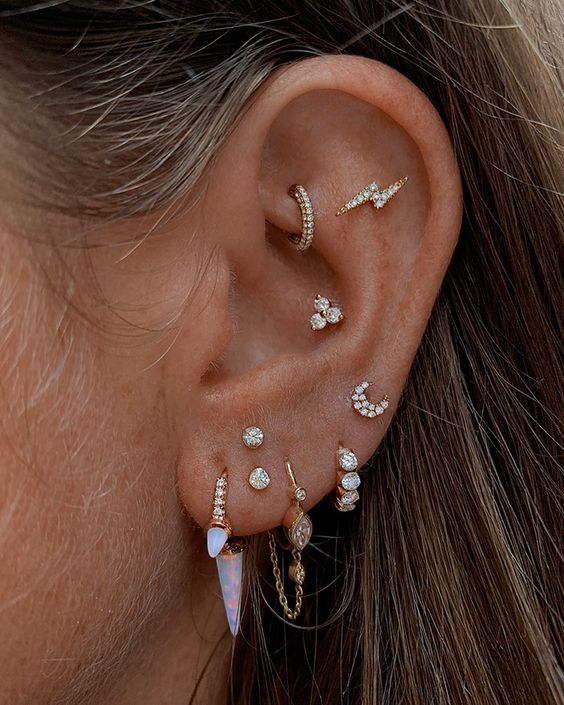 a gorgeous ear look with a rook, conch, flat, stacked lobe and high lobe piercings done with catchy studs and hoops