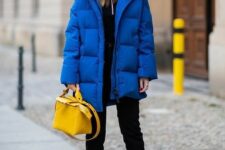 a sport chic winter look with a black zip sweater and jeans, black boots with blue laces, a blue puffer jacket and a yellow bag