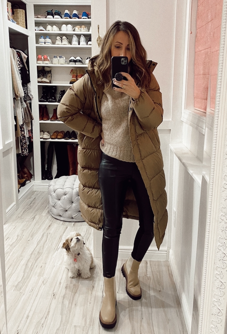 a stylish winter outfit with a beige sweater, black leather pants, beige Chelsea boots, a beige puffer coat