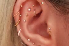 a super bold ear with a double forward helix and tragus, multiple flat, lobe and helix piercings with lots of gold studs and hoops