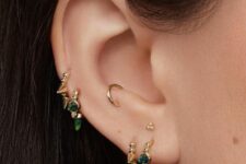 a triple lobe, a snug and a double mid helix piercing done with gold and emerald hoops and a small gold stud