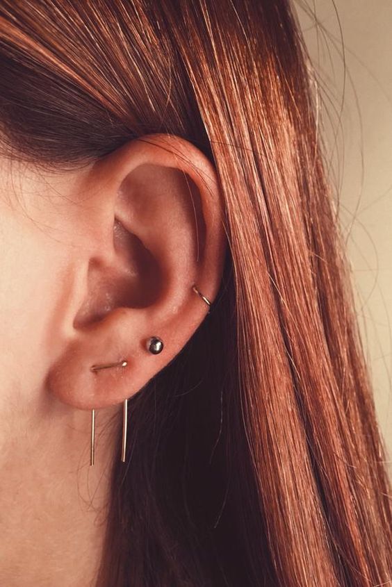 a triple lobe and a mid helix piercing done with gold hoops, chain and a black pearl earrings are wow