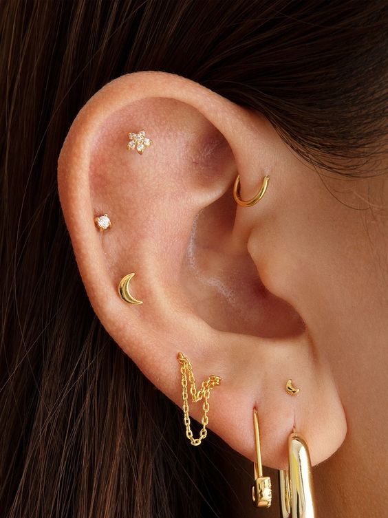 a triple lobe, double mid helix, a flat and a forward helix piercings done with gold chain, hoops and studs with rhinestones