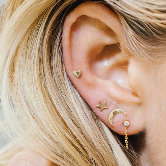 a triple lobe piercing and a mid helix done with gold studs and chain are a bold and cool idea