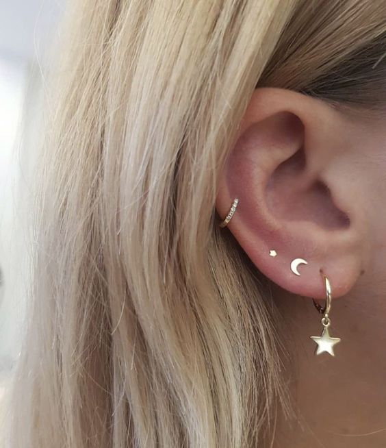 a triple lobe piercing done with gold studs and a hoop with a star, a mid helix piercing with a rhinestone hoop
