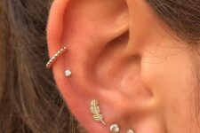 a triple lobe piercing done with rhinestone studs and a feather, a double mid helix piercing with a stud and a hoop
