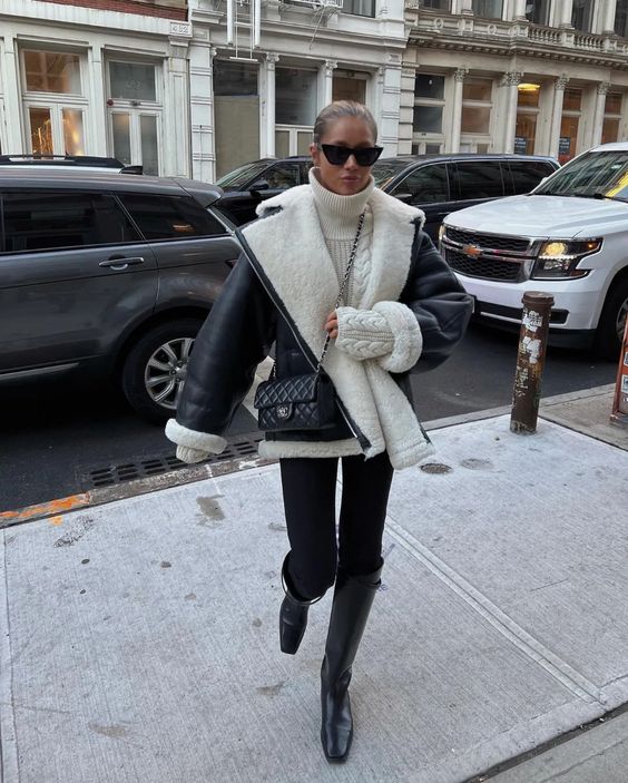 a white sweater, black skinnies tucked into knee boots, a black and white aviator coat and a black bag