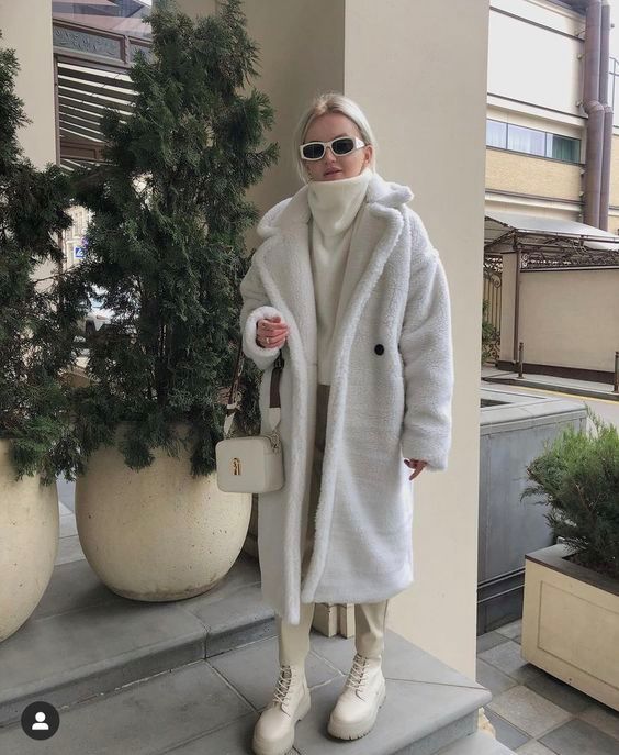 an all-white winter look with a sweater, boots, a faux fur coat, a bag and beige leather pants is very chic