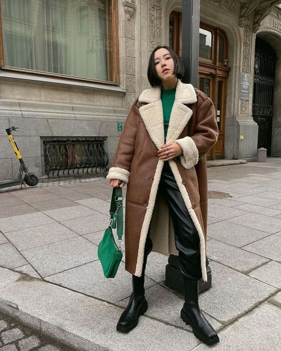 an emerald turtleneck, black leather pants, black boots, a brown shearling coat, an emerald bag