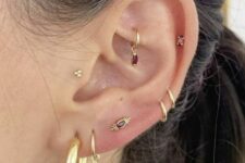 bold ear style with a triple lobe, double mid helix, upper helix, rook and tragus piercings, with gold hoops and studs with burgundy rhinestones