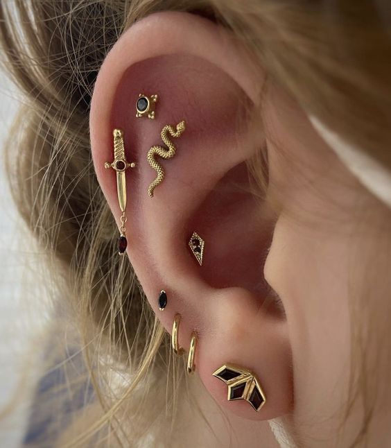bold ear styling done with stacked lobe, high lobe, stacked flat and conch piercings with catchy gold and emerald studs