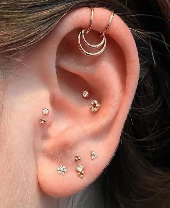 bold ear styling with multiple lobe, double tragus, double conch and double helix piercings done with gold studs and hoops