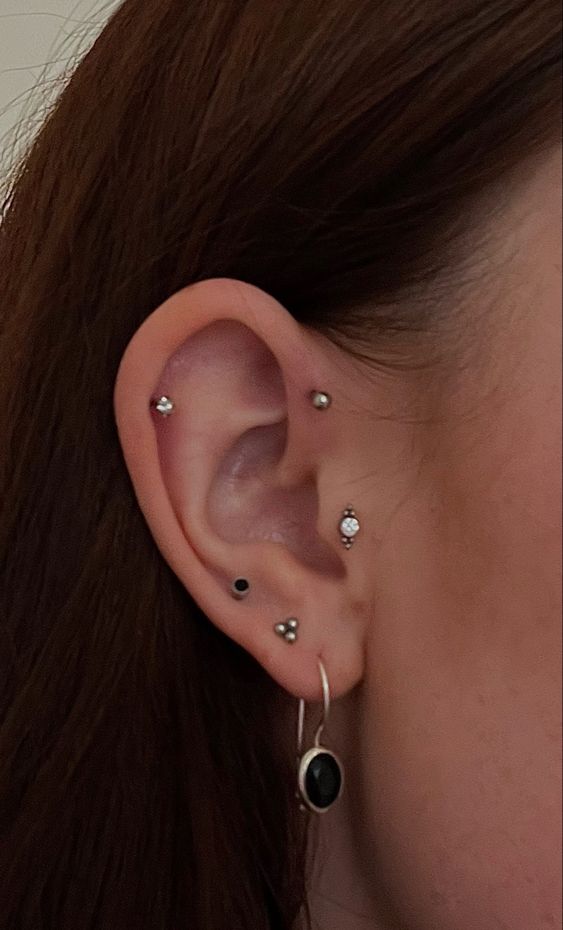 chic and modern ear styling done with a tragus, forward and usual helix plus stacked lobe and high lobe piercing and lovely studs and a hoop