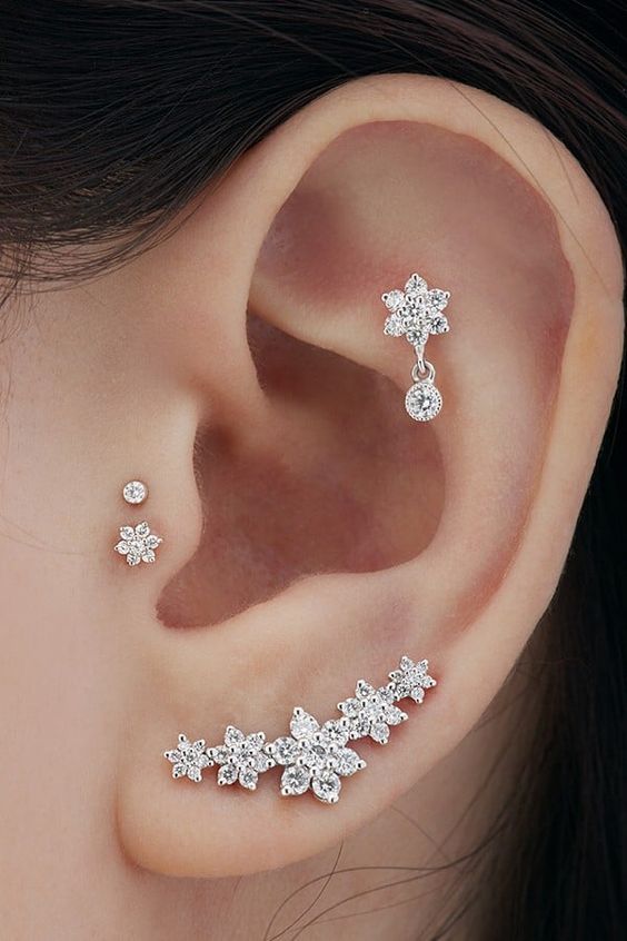 glam ear styling with a lobe, double tragus and a flat piercing done with chic flower-shaped studs of various sizes