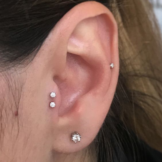 minimalist ear styling with a double tragus, a lobe and a mid-helix piercing done with matching white rhinestone studs