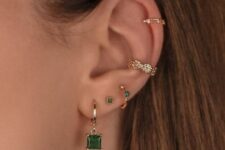 stacked ear piercings including lobe, conch and helix ones, with hoops and studs with emeralds look amazing
