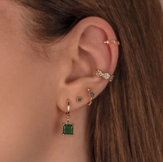 stacked ear piercings including lobe, conch and helix ones, with hoops and studs with emeralds look amazing