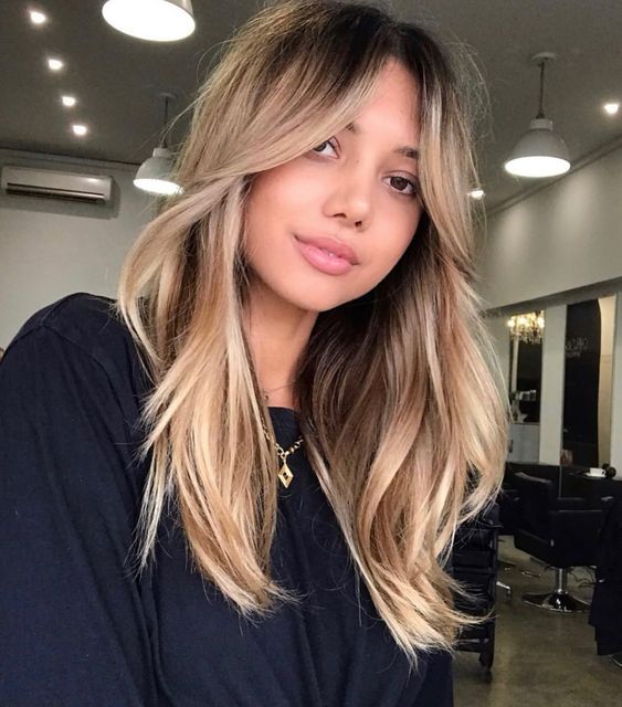 long hair with a darker root and blonde balayage and curtain bangs, with waves and volume is cool