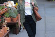 Reese Witherspoon wearing a graphic tee, black cuffed jeans, clogs, a utility jacket and a brown tote