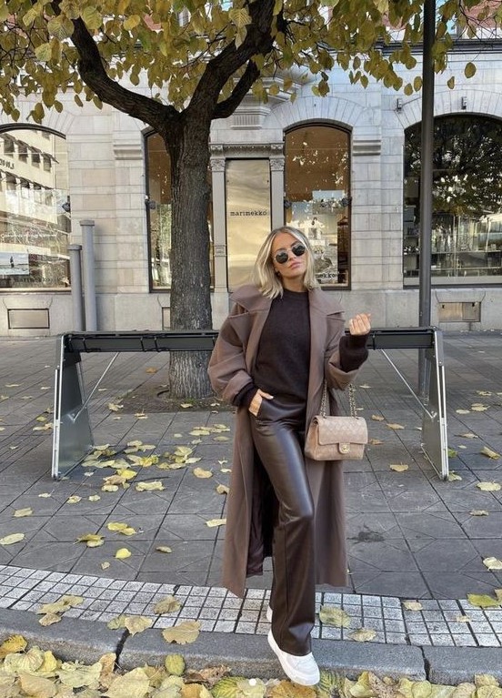 a black jumper, brown leather flare pants, a taupe coat, white trainers, a beige bag compose a monochromatic work look