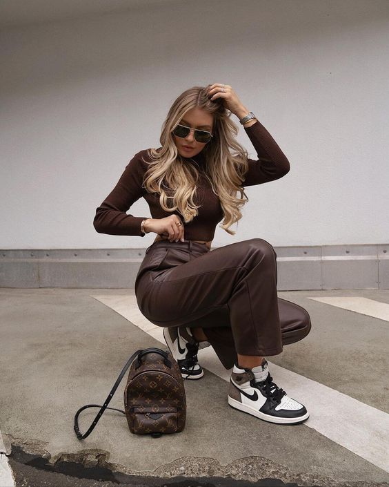 a brown long sleeve crop top, brown leather pants, black and white trainers and a brown printed bag for rocking this spring