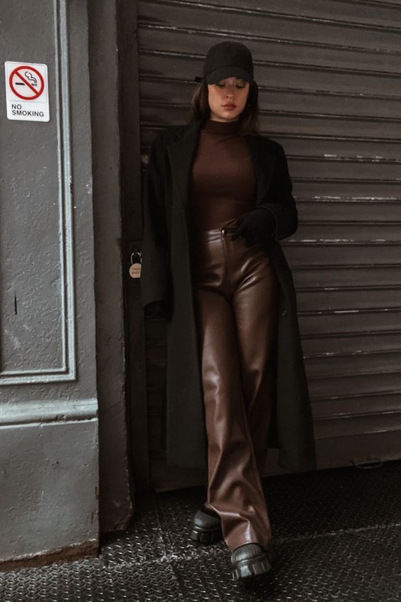 a brown turtleneck, brown leather trousers, black chunky boots, a black midi coat and a cap for a cozy winter look