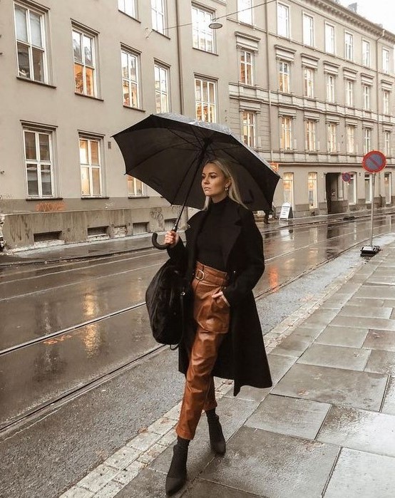 a chic look with a black turtleneck, brown leather pants, sock boots, a black coat and a bag