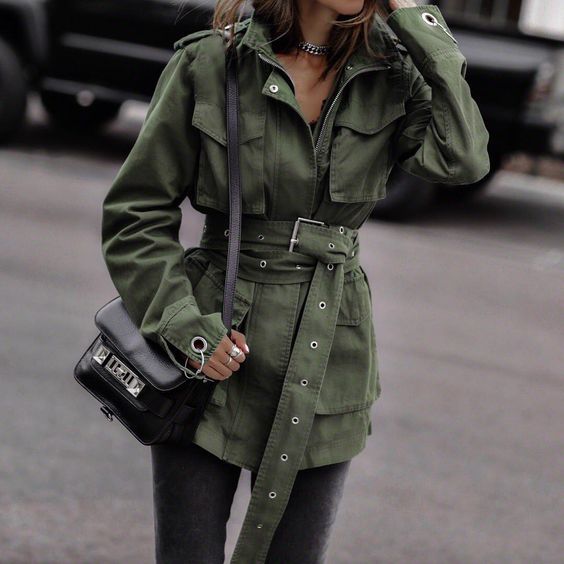 a green belted utility jacket, grey jeans, a black bag and statement accessories for a dramatic look
