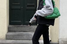 a grey hoodie, black flare jeans, a black puffer vest, a bold green embossed bag are a cool and comfy look for the transition
