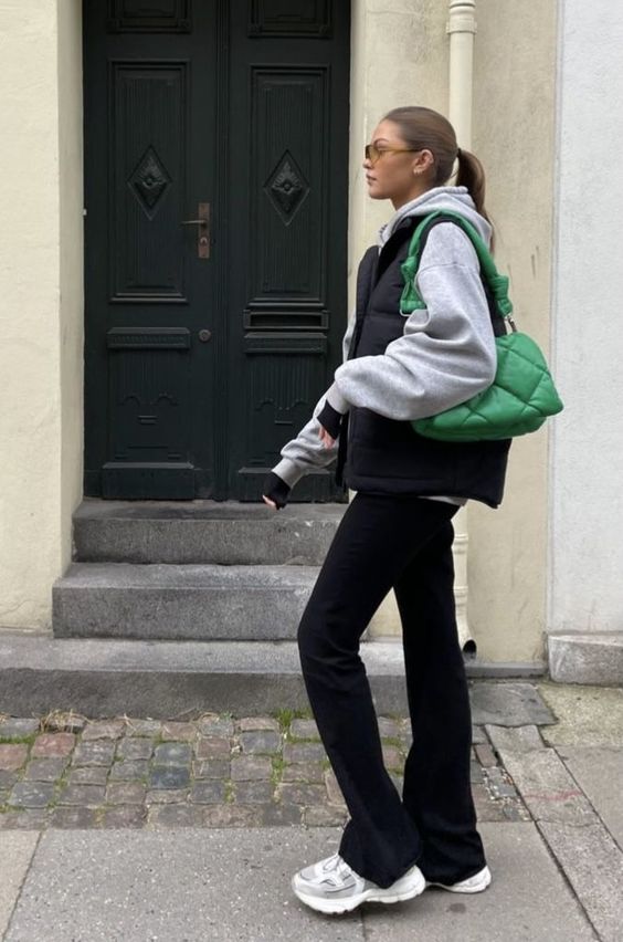 a grey hoodie, black flare jeans, a black puffer vest, a bold green embossed bag are a cool and comfy look for the transition