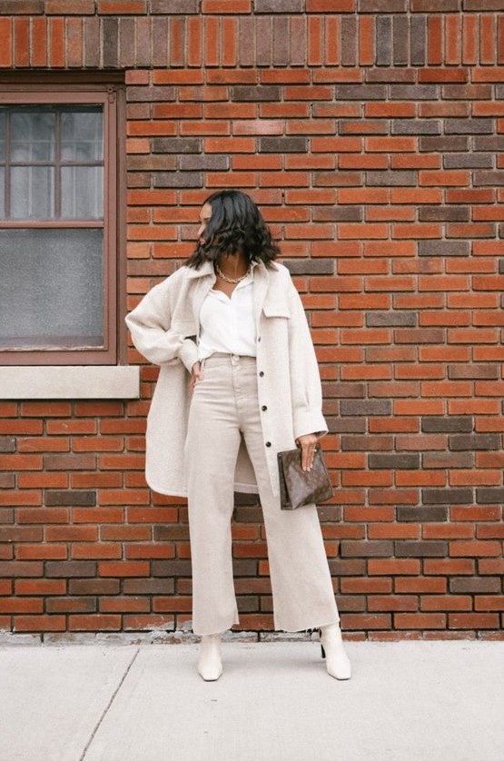 a neutral fall work look with a white shirt, off-white wideleg jeans, a shirt jacket, white boots and a brown clutch