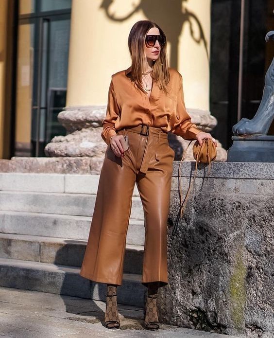 a rust-colored blouse, brown cropped leather pants, printed socks and black shoes plus an elegant bag for a special occasion