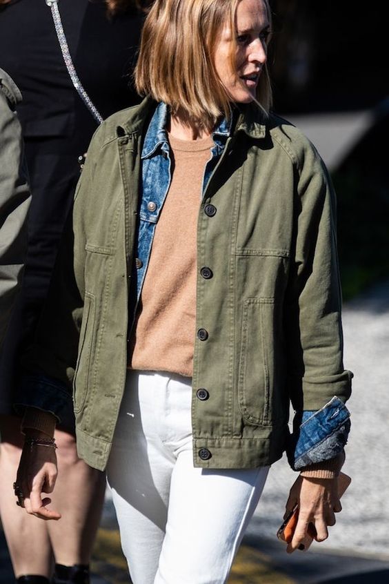 a tan top, a blue denim shirt, a green utility jacket and white jeans for a layering look