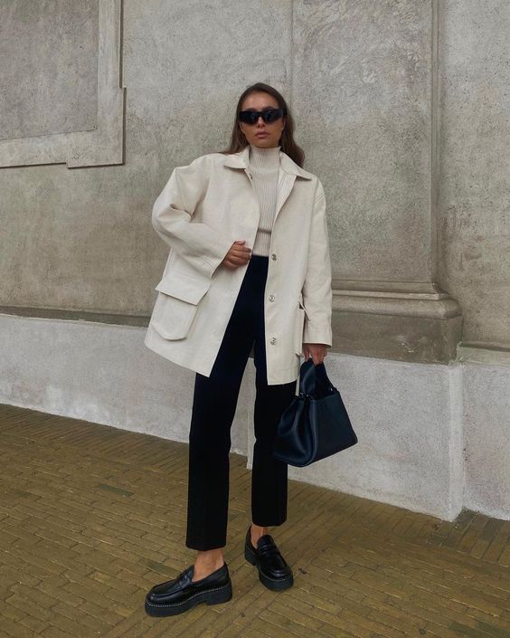 a white turtleneck and shirt jacket, black pants, black loafers and a bag for a polished monochromatic look