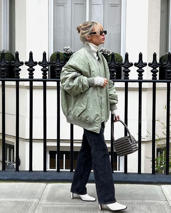 a white turtleneck and white boots, an olive green bomber jacket, black flare jeans and a printed bag