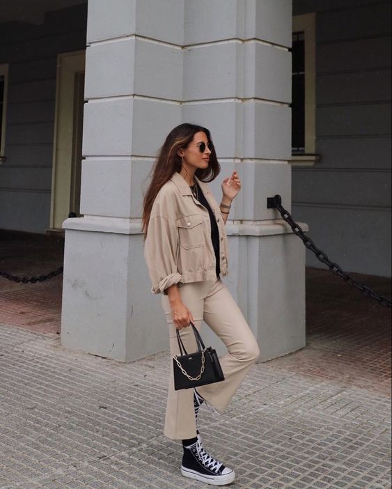 a black tee, beige flare pants, a tan cropped denim jacket, black sneakers and a small black bag