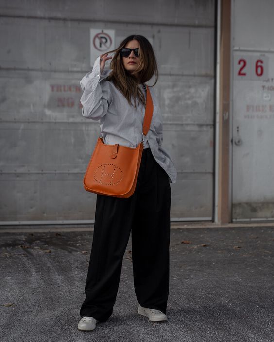 a minimalist look with an oversized grey shirt, wide leg trousers, white sneakers and a cool and bright orange tote