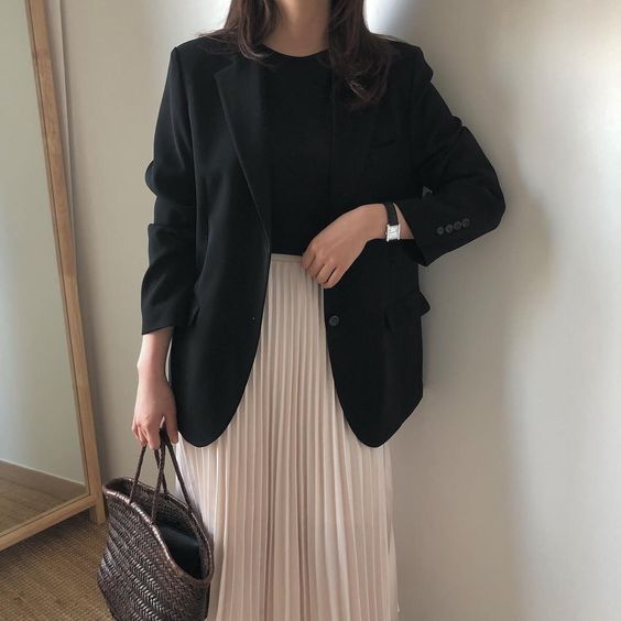 a black t-shirt, a black blazer, a blush pleated midi, a straw tote and a watch are an elegant work look for spring